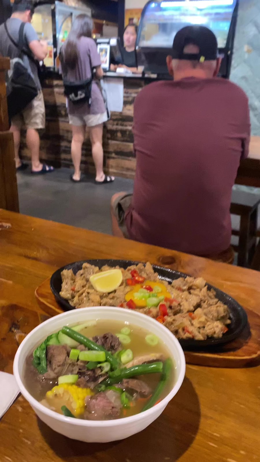 Sizzling sisig and a bowl of bulalo on a timber table in the food hall